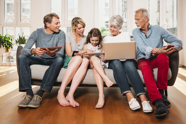 Gruppenbild einer Familie mit drei Generationen und verschiedenen digitalen Geräten, die auf einer Couch sitzen - MFF001750