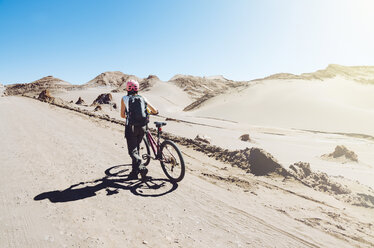 Chile, Frau, die ein Mountainbike durch das Mondtal in der Atacama-Wüste schiebt - GEMF000256