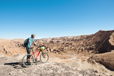 Chile, Man holding a mountain bike and looking to the Death Valley in the Atacama Desert - GEMF000259