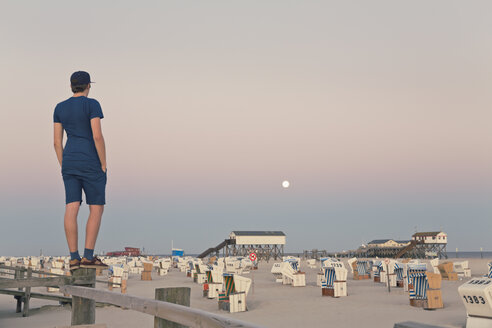 Deutschland, St. Peter-Ording, junger Mann steht am Holzzaun und schaut auf den Strand - MEMF000817