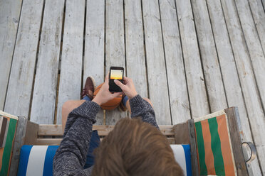 Jugendlicher mit Basketball und Smartphone in einem Strandstuhl mit Kapuze - MEMF000833