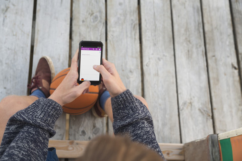 Teenage boy with basketball using smartphone stock photo