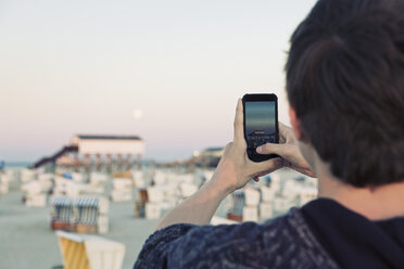 Germany, St Peter-Ording, teenage boy taking picture of full moon with his smartphone - MEMF000830