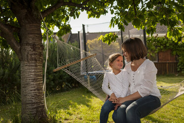 Mutter und ihre kleine Tochter sitzen in einer Hängematte im Garten - PAF001448