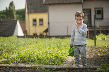 Nachdenklicher kleiner Junge mit Kindergießkanne im Garten stehend - PAF001451