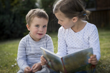 Girl and her little brother sitting on a meadow with a picture book - PAF001459