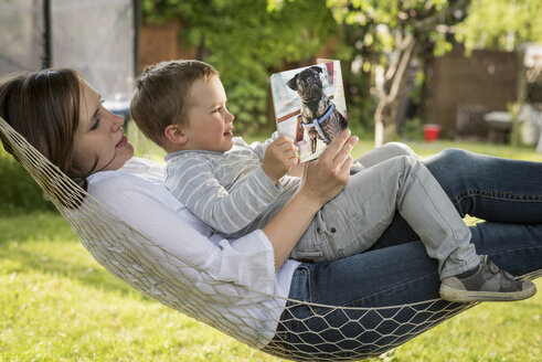 Mutter und ihr kleiner Sohn entspannen sich gemeinsam in einer Hängematte im Garten - PAF001465