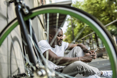 Porträt eines jungen Mannes, der hinter einem Fahrrad sitzt und mit einem Smartphone telefoniert - RIBF000117