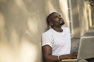 Porträt eines jungen Mannes, der mit seinem Laptop auf dem Boden sitzt - RIBF000119