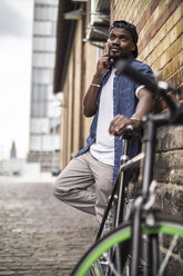 Germany, Cologne, portrait of young man with bicycle telephoning with smartphone - RIBF000130