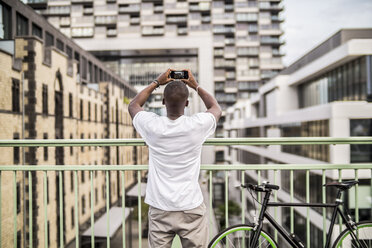 Deutschland, Köln, junger Mann beim Fotografieren mit Smartphone - RIBF000134