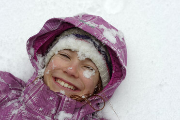 Porträt eines lächelnden Mädchens auf Schnee liegend - LBF001140