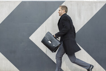 Businessman with briefcase running along wall - WESTF021282