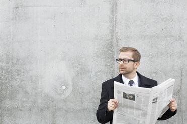 Businessman with newspaper at concrete wall - WESTF021294