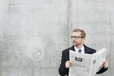 Geschäftsmann mit Zeitung an Betonwand - WESTF021294