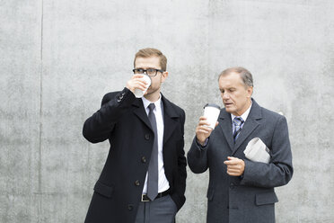 Zwei Geschäftsleute mit Kaffee zum Mitnehmen an einer Betonwand - WESTF021298