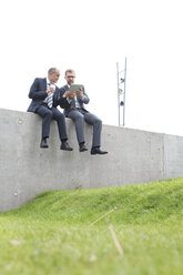 Zwei Geschäftsleute mit digitalem Tablet sitzen an einer Betonwand - WESTF021308