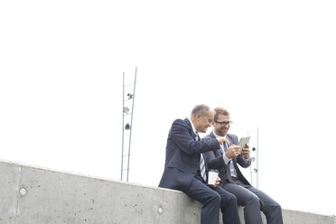 Zwei Geschäftsleute mit digitalem Tablet sitzen an einer Betonwand - WESTF021309