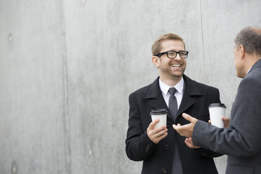 Zwei lächelnde Geschäftsleute mit Kaffee zum Mitnehmen an einer Betonwand - WESTF021323