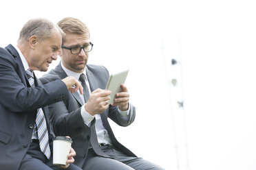 Two businessmen with digital tablet and coffee to go outdoors - WESTF021368
