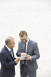 Two businessmen with digital tablet standing on square - WESTF021341