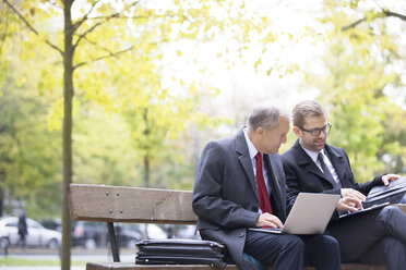 Two businessmen with laptop and documents on park bench - WESTF021375