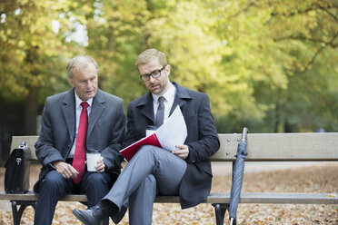 Zwei Geschäftsleute lesen ein Dokument auf einer Parkbank - WESTF021350