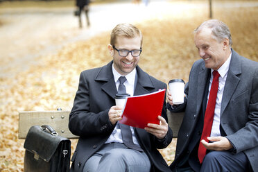 Zwei glückliche Geschäftsleute mit Dokument und Kaffee zum Mitnehmen auf einer Parkbank - WESTF021349