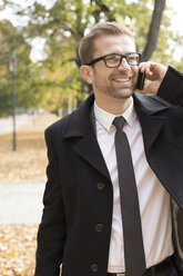 Lächelnder Geschäftsmann in einem Park beim Telefonieren - WESTF021354