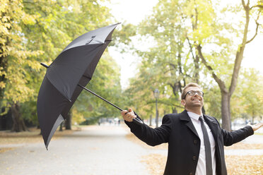 Glücklicher Geschäftsmann in einem Park mit Regenschirm nach Regen - WESTF021359