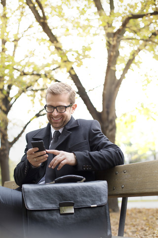 Smiling businessman on park bench looking at cell phone stock photo