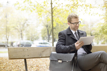 Smiling businessman on park bench using digital tablet - WESTF021362