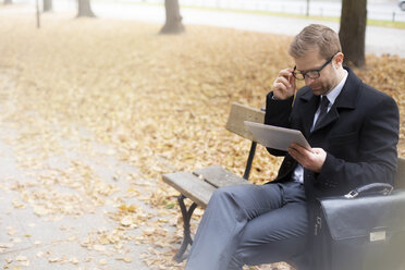 Businessman on park bench using digital tablet - WESTF021380
