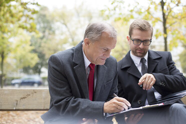 Geschäftsmann mit Partner, der auf einer Parkbank ein Dokument unterzeichnet - WESTF021363