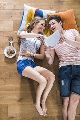 Happy young couple lying on floor sharing digital tablet - UUF004839