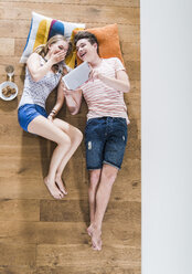 Glückliches junges Paar liegt auf dem Boden und teilt sich ein digitales Tablet - UUF004840