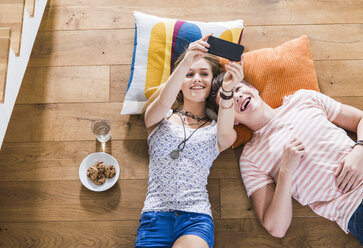 Happy young couple lying on floor looking at cell phone - UUF004842