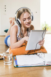 Teenage girl lying on floor listening to music from digital tablet - UUF004847