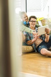 Glückliches junges Paar zu Hause, das sich ein digitales Tablet teilt - UUF004852