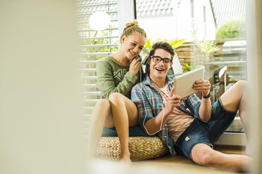 Glückliches junges Paar zu Hause, das sich ein digitales Tablet teilt - UUF004853