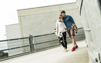 Happy young couple walking with skateboards - UUF004887