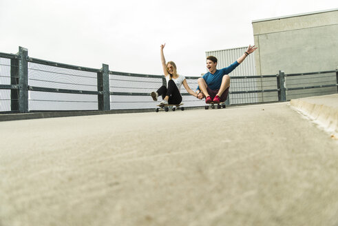 Enthusiastisches junges Paar fährt mit Skateboards bergab - UUF004889