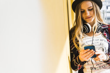 Teenage girl leaning against wall looking at cell phone - UUF004896