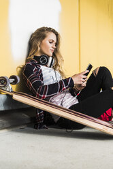 Teenage girl sitting on floor with skateboard and cell phone - UUF004898