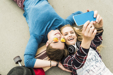 Happy young couple lying on ground with skateboard looking at cell phone - UUF004900