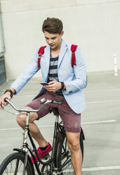 Junger Mann mit Fahrrad schaut auf sein Handy - UUF004901