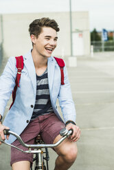 Fröhlicher junger Mann fährt Fahrrad auf einem Parkdeck - UUF004903