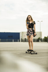 Teenager-Mädchen fährt Skateboard und schaut auf ein Handy - UUF004913