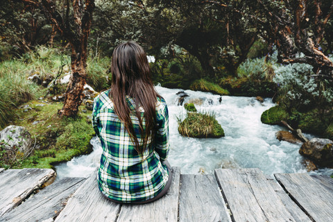 Peru, junge Frau sitzt auf einer Holzbrücke und genießt die Natur, lizenzfreies Stockfoto