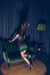 Back view of young woman kneeling on couch tossing her hair - CHAF000533
